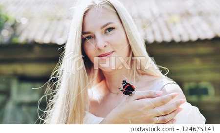 Beautiful blonde woman holding a butterfly on her hand in summer sunlight, enjoying nature and wildlife 124675141