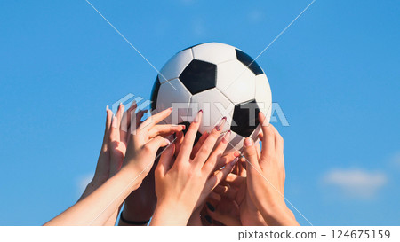 School friends holding soccer ball together under blue sky, showing teamwork and sportsmanship 124675159