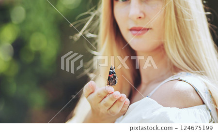 Smiling blonde woman gently cradling delicate butterfly amidst lush garden greenery 124675199