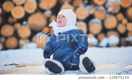 Bundled infant resting on wooden logs, smiling amid snowy landscape, wearing cozy winter outerwear during cold seasonal moment 124675239