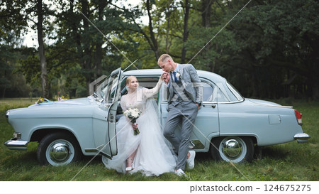 Romantic newlyweds celebrating their wedding day with a vintage car in a picturesque outdoor setting Romantic newlyweds celebrating their wedding day with a vintage car in a picturesque outdoor setting 124675275
