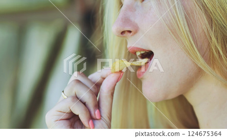 Close up of a young blond woman savoring a potato chip, highlighting the simple pleasure of enjoying a crispy snack Close up of a young blond woman savoring a potato chip, highlighting the simple pleasure of enjoying a crispy snack 124675364