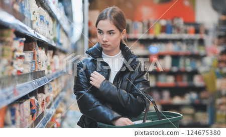 Shopper comparing products, selecting groceries in supermarket aisle, holding basket 124675380