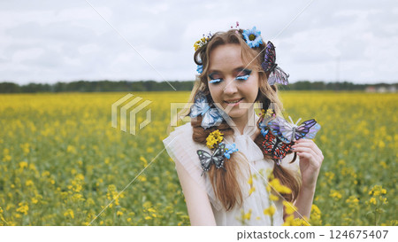 Fashion model wearing butterfly and flower decorations in a canola field, enjoying a sunny summer day 124675407