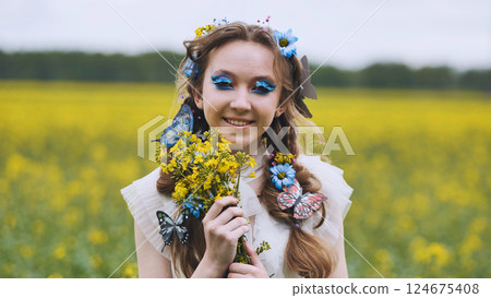 Smiling young model wearing butterfly hair decor, holding yellow bouquet among vibrant canola field blossoms Smiling young model wearing butterfly hair decor, holding yellow bouquet among vibrant canola field blossoms 124675408