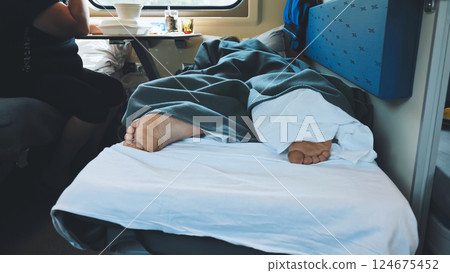 Bare feet resting on a train bunk while another passenger enjoys a meal nearby, creating a cozy atmosphere during the journey 124675452