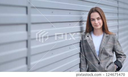 Confident businesswoman in stylish plaid blazer posing against a modern metal wall, showcasing urban professional style 124675470