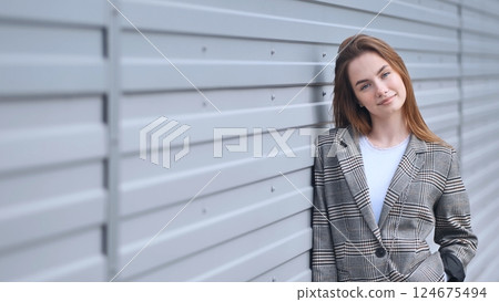 Professional businesswoman standing near gray metal wall, wearing sleek office attire, embodying contemporary urban workplace style 124675494