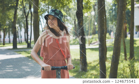 Teenage girl gliding through sunlit park on electric scooter, embracing eco friendly urban mobility and carefree summer enjoyment 124675541