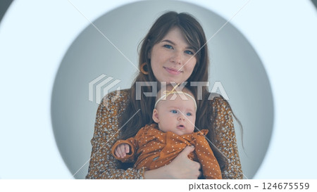 Young mother cuddling her baby daughter inside a luminous circle, creating a tender and intimate moment 124675559