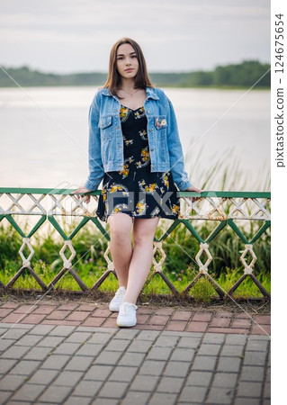 Fashionable student posing by a lake, enjoying a peaceful summer day surrounded by nature Fashionable student posing by a lake, enjoying a peaceful summer day surrounded by nature 124675654