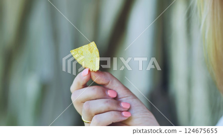 Well groomed female hand grasping single golden potato chip, anticipating savory crisp snacking experience Well groomed female hand grasping single golden potato chip, anticipating savory crisp snacking experience 124675655