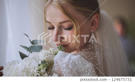 Elegant bride inhaling white wedding bouquet with eucalyptus, groom softly blurred in background Elegant bride inhaling white wedding bouquet with eucalyptus, groom softly blurred in background 124675731