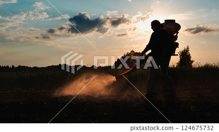Farmer walking on cultivated field spraying pesticides with manual knapsack sprayer at sunset Farmer walking on cultivated field spraying pesticides with manual knapsack sprayer at sunset 124675732