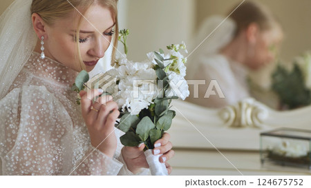 Bride wearing white wedding dress holding and smelling white flowers bouquet getting ready on her wedding day Bride wearing white wedding dress holding and smelling white flowers bouquet getting ready on her wedding day 124675752