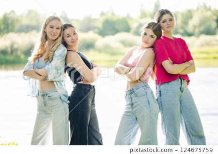 Four female students stand back to back, arms crossed, enjoying a sunny day by the riverbank Four female students stand back to back, arms crossed, enjoying a sunny day by the riverbank 124675759