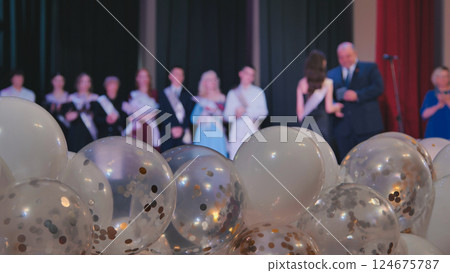 White and transparent balloons filled with gold and silver confetti celebrate graduation, surrounded by blurred friends and teachers White and transparent balloons filled with gold and silver confetti celebrate graduation, surrounded by blurred friends and teachers 124675787