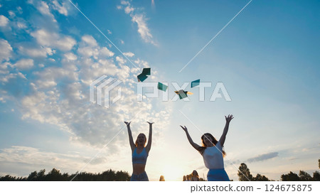 Two cheerful students throwing books in the air, celebrating graduation with friends at sunset 124675875