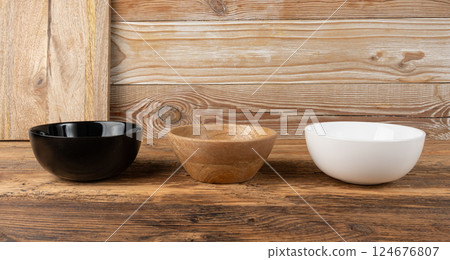 Three empty bowls on table, white porcelain, black and wooden dishes on tabletop, rustic dish 124676807