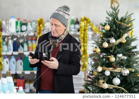 In X mas atmosphere, senior man sniffs fragrance of perfume, chooses scent spray with pleasant smell In X mas atmosphere, senior man sniffs fragrance of perfume, chooses scent spray with pleasant smell 124677351