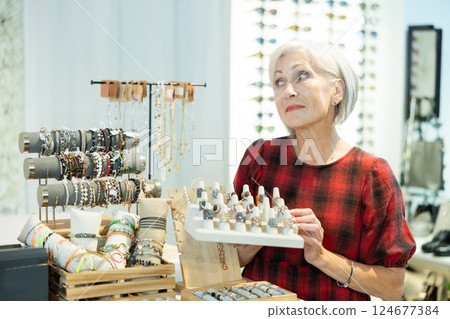 Elderly woman client enthusiastically examines showcase counter with jewelry 124677384
