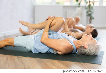 Three generations of women do preparatory stretching, lying on back and benting one leg at knee Three generations of women do preparatory stretching, lying on back and benting one leg at knee 124677625
