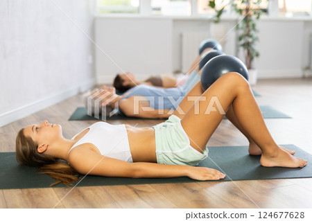 Fitness family in activewear working out with soft ball pilates on mat while doing upper body training in yoga studio Fitness family in activewear working out with soft ball pilates on mat while doing upper body training in yoga studio 124677628