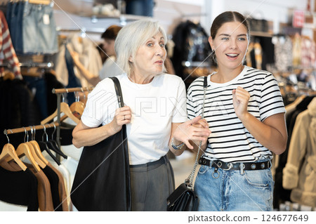 Two women watching excitedly large stock of clothes in clothing store 124677649