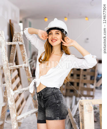 Sensual long-haired woman in hardhat, shirt and shorts posing in room under renovation 124677904