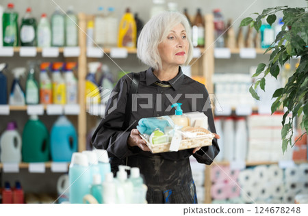 Elderly woman chooses gift set of shampoo, liquid soap and cosmetic items in supermarket 124678248