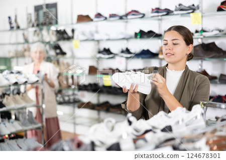 Young woman chooses sneakers in shoe store Young woman chooses sneakers in shoe store 124678301