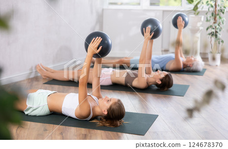 Teenage girl doing pilates with soft ball in group Teenage girl doing pilates with soft ball in group 124678370