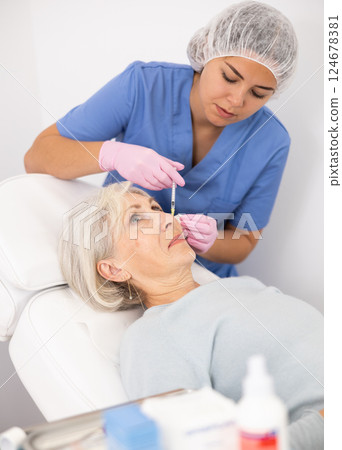 Young female doctor cosmetologist making rejuvenating injections procedure for tightening and smoothing wrinkles on face skin of old woman in beauty salon 124678381