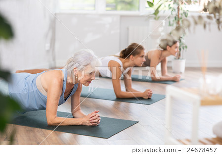 Three generations of women perform elbow plank Sampatasana in gym 124678457
