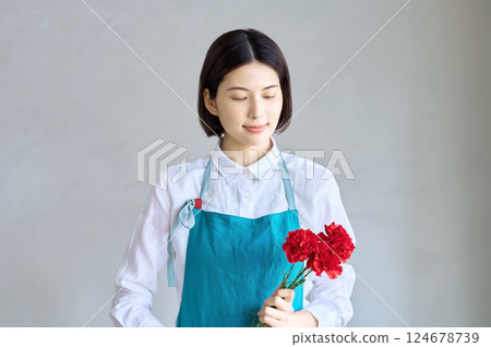 一位年輕的家庭主婦穿著圍裙，手裡拿著一朵康乃馨 124678739