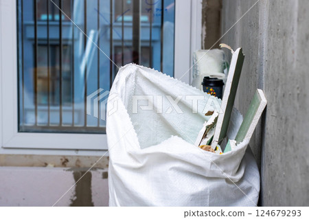 A white bag full of items is leaning against a wall A white bag full of items is leaning against a wall 124679293