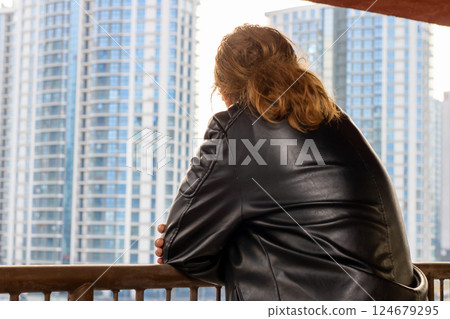 A woman in a stylish leather jacket gazes over a sprawling city A woman in a stylish leather jacket gazes over a sprawling city 124679295