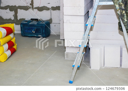 A bright blue toolbox is located on the floor beside a ladder 124679306