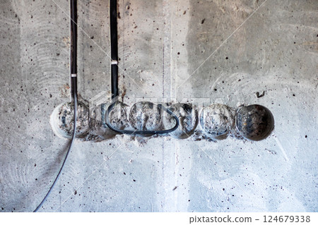 A mess of wires is suspended from an exposed concrete wall surface 124679338
