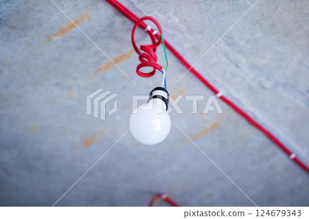 A single light bulb is hanging gracefully from a bright red cord 124679343
