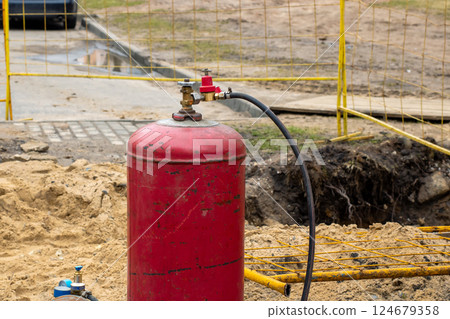 A red gas cylinder with an attached hose sits in the dirt A red gas cylinder with an attached hose sits in the dirt 124679358