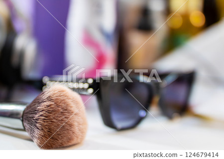 A makeup brush and a stylish pair of sunglasses are on a table A makeup brush and a stylish pair of sunglasses are on a table 124679414