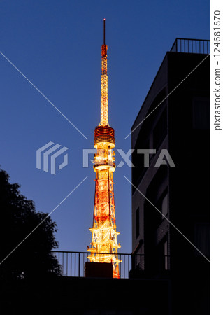 Tokyo Tower rises above the city framed by dark residential buildings with its golden lights 124681870