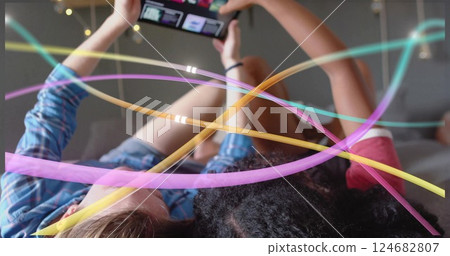Colorful light trails image over people lying down and using tablet 124682807