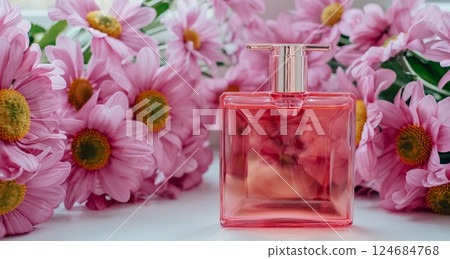 Elegant pink perfume bottle placed on a white surface surrounded by beautiful blooming pink daisies Elegant pink perfume bottle placed on a white surface surrounded by beautiful blooming pink daisies 124684768