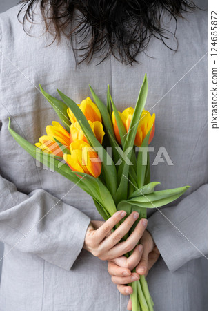 woman holds bouquet of yellow-red tulips in hands. birthday or mother's day gift. view from back. woman holds bouquet of yellow-red tulips in hands. birthday or mother's day gift. view from back. 124685872