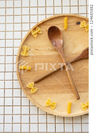 time to eat pasta. wooden plate with fork and spoon in form of clock hands. pasta on plate. 124685882