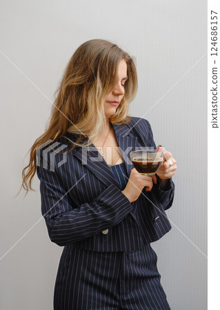 Businesswoman enjoys coffee while dressed in a stylish pinstriped suit Businesswoman enjoys coffee while dressed in a stylish pinstriped suit 124686157