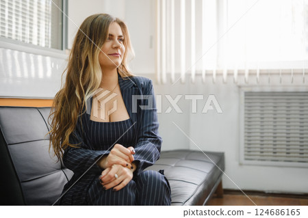 Woman in a pinstripe suit sitting on a couch in a bright, modern office setting Woman in a pinstripe suit sitting on a couch in a bright, modern office setting 124686165