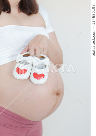 Pregnant Woman Showcasing Baby Shoes with Heart Details on Bare Belly Pregnant Woman Showcasing Baby Shoes with Heart Details on Bare Belly 124686198